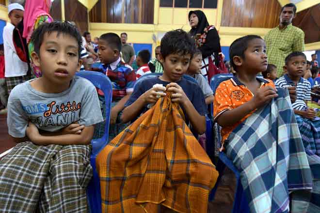 Tiga orang anak lelaki berkain pelikat sedang duduk menunggu giliran untuk berkhatan